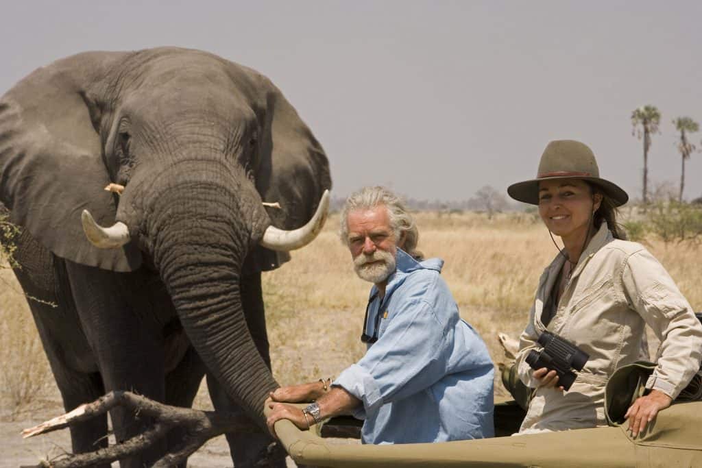 Wildlife Filmmakers Dereck and Beverly Joubert inside their production 4x4 vehicle near an adult elephant.